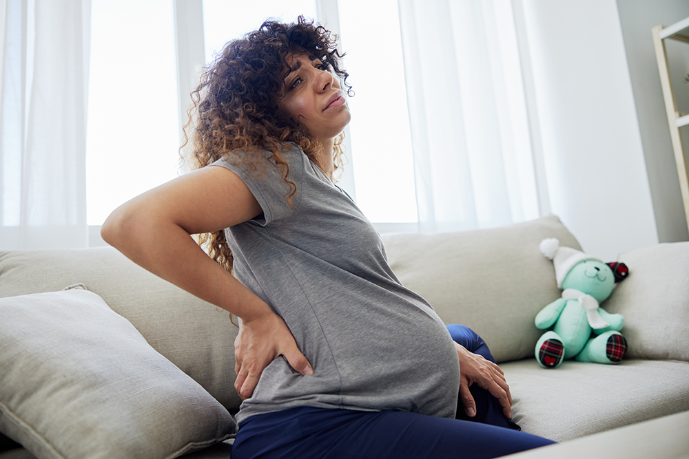 5 PT techniques that can improve SI joint pain while pregnant pregnant woman sitting on the couch lower back pai 2023 12 19 07 01 11 utc 1 5 PT techniques that can improve SI joint pain while pregnant